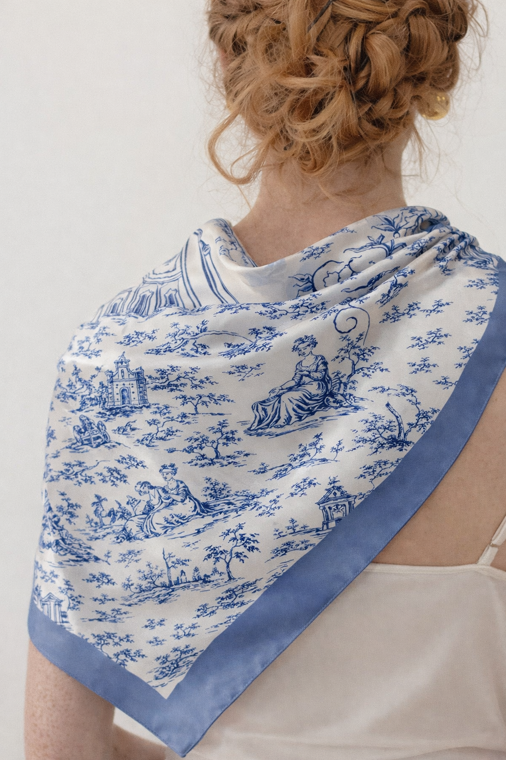 Foulard en soie bleu à motif toile de Jouy porté sur les épaules, détail du tombé naturel et de la fluidité de la matière